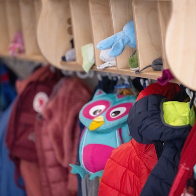 Bunte Jacken und Taschen hängen an einer Garderobe einer Kita.