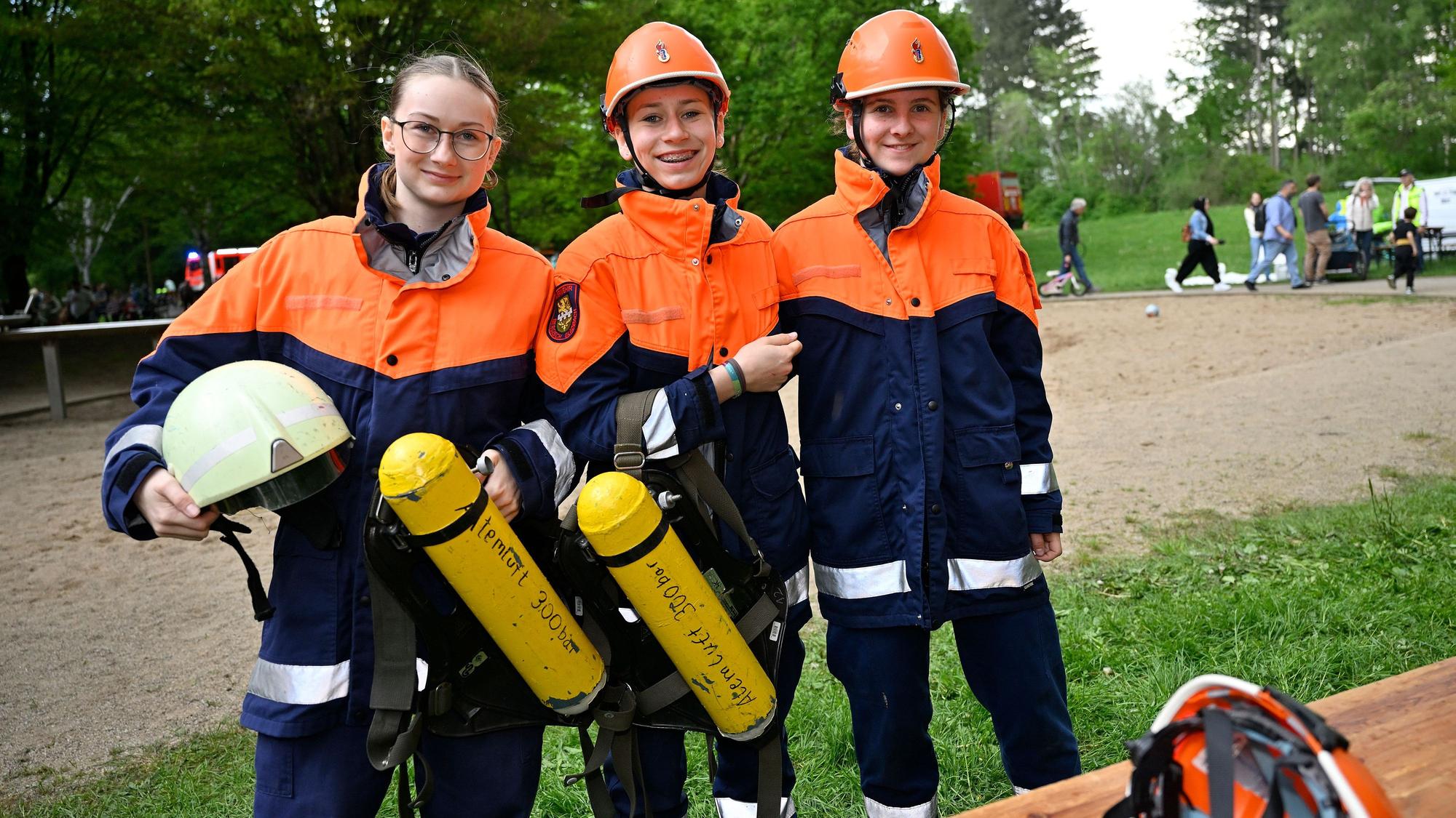 Drei Jugendfeuerwehrleute stehen nebeneinander und halten einen Helm sowie Pressluftatemflaschen.