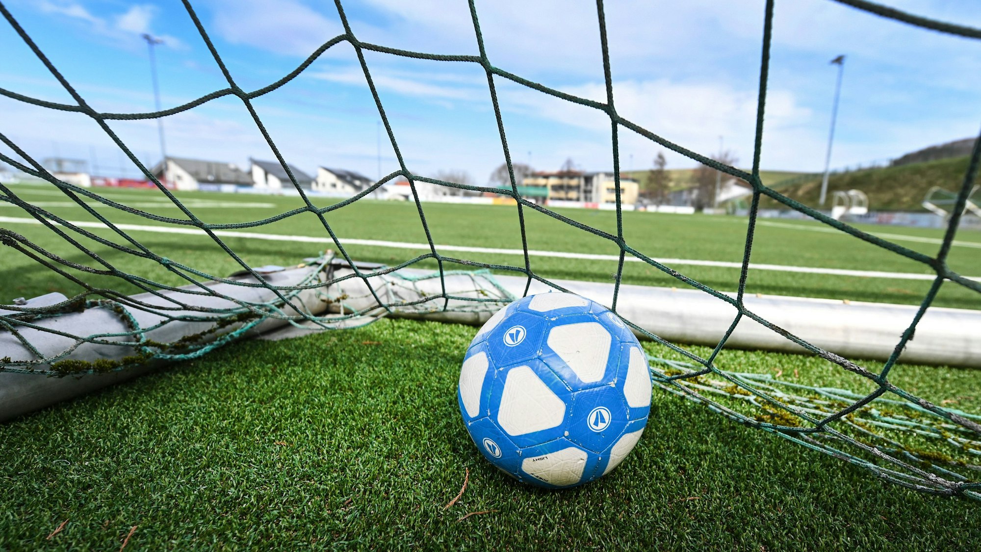 Ein Fußball liegt in einem Tor, das auf einem leeren Fußballplatz steht.