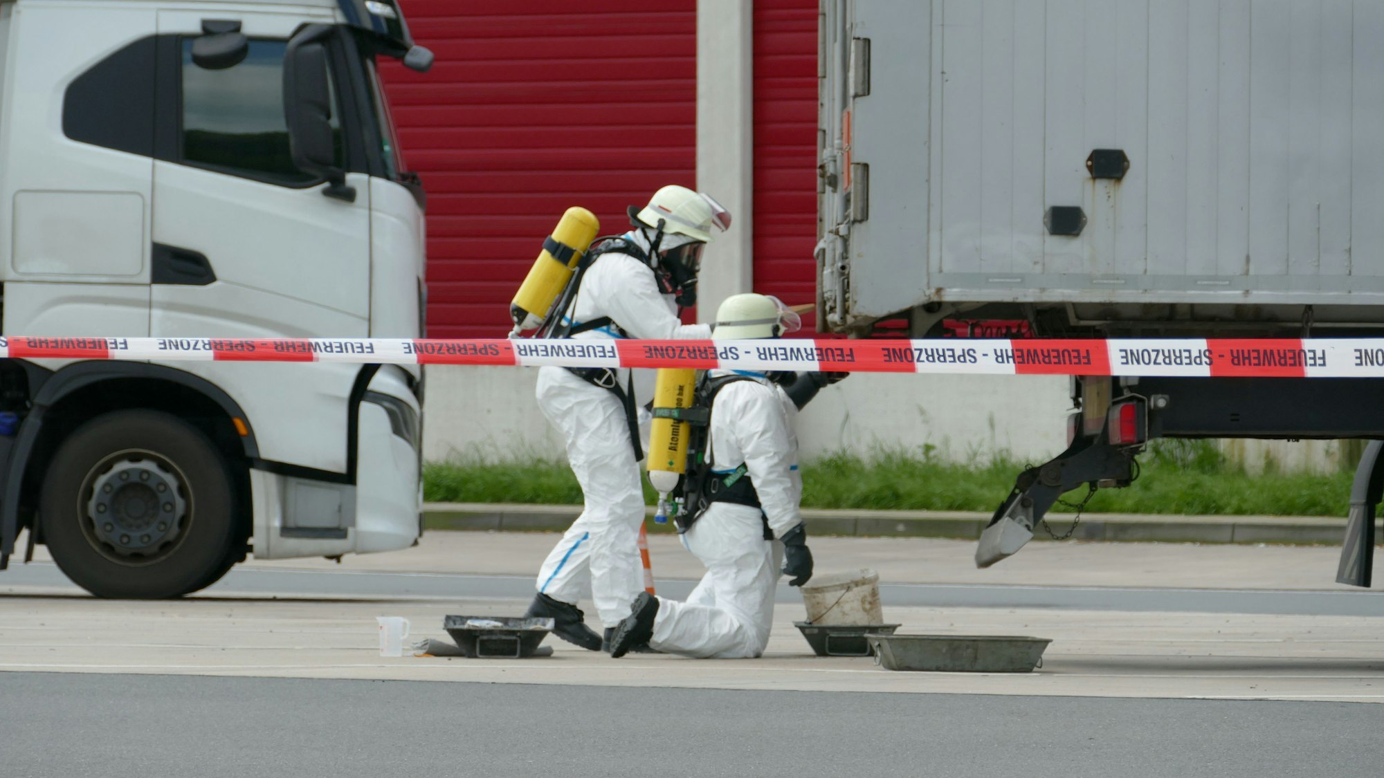 Feuerwehrleute in Schutzanzügen stellen Auffangbehälter unter den Lkw.
