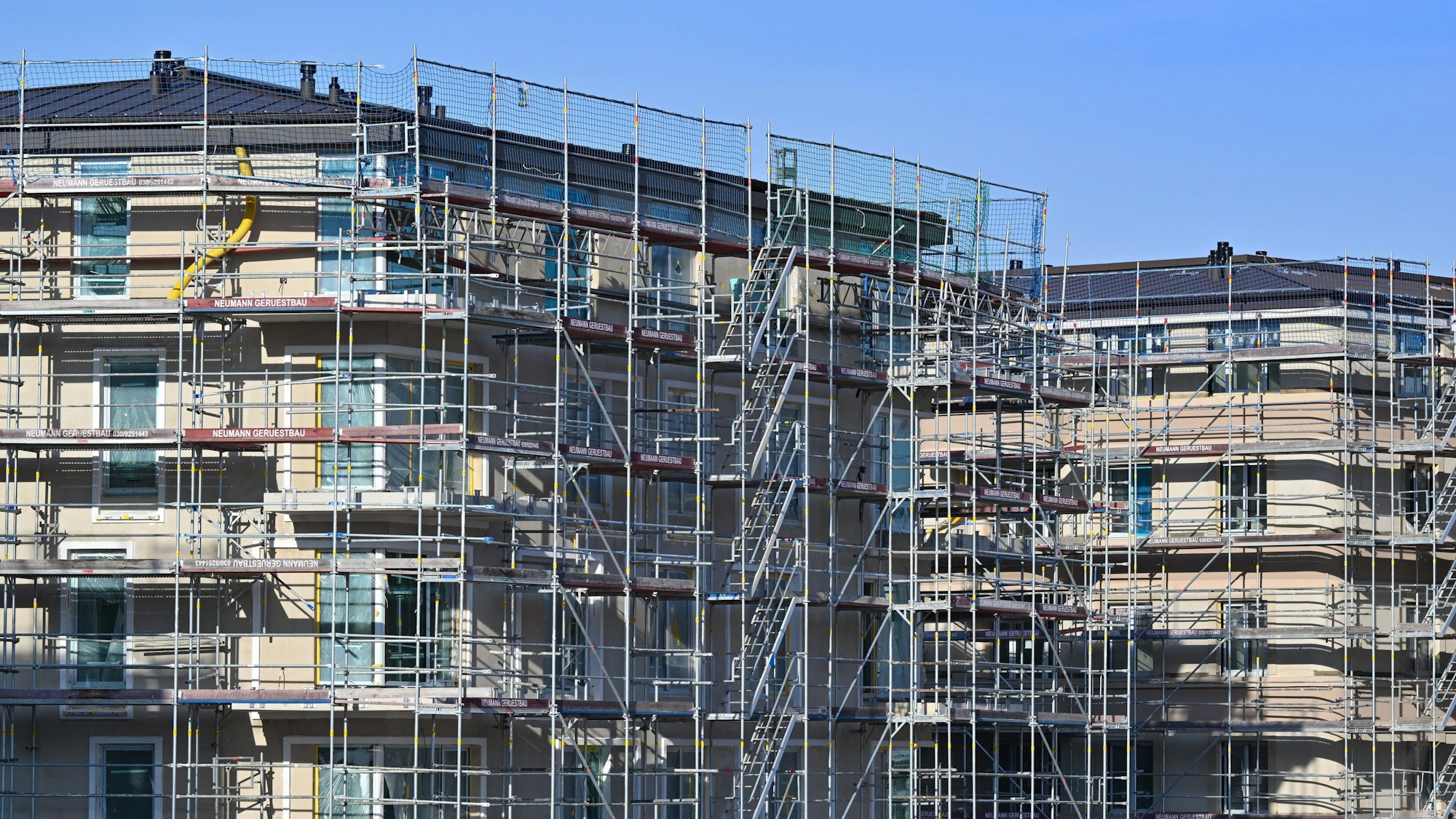 Neue Wohnhäuser, noch mit Gerüsten ummantelt, vor einem blauen Himmel.