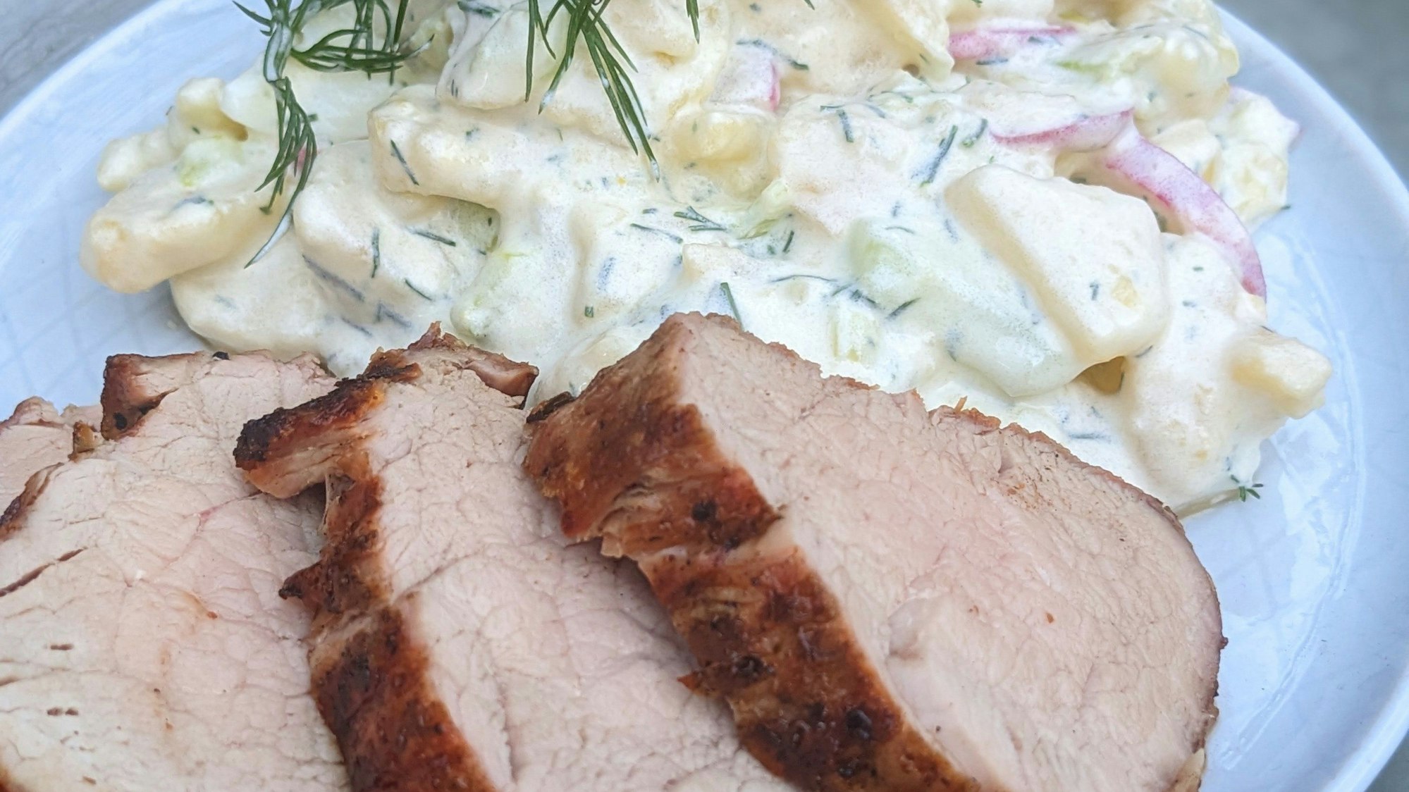 Auf einem Teller liegt Schweinefilet und Kartoffelsalat.