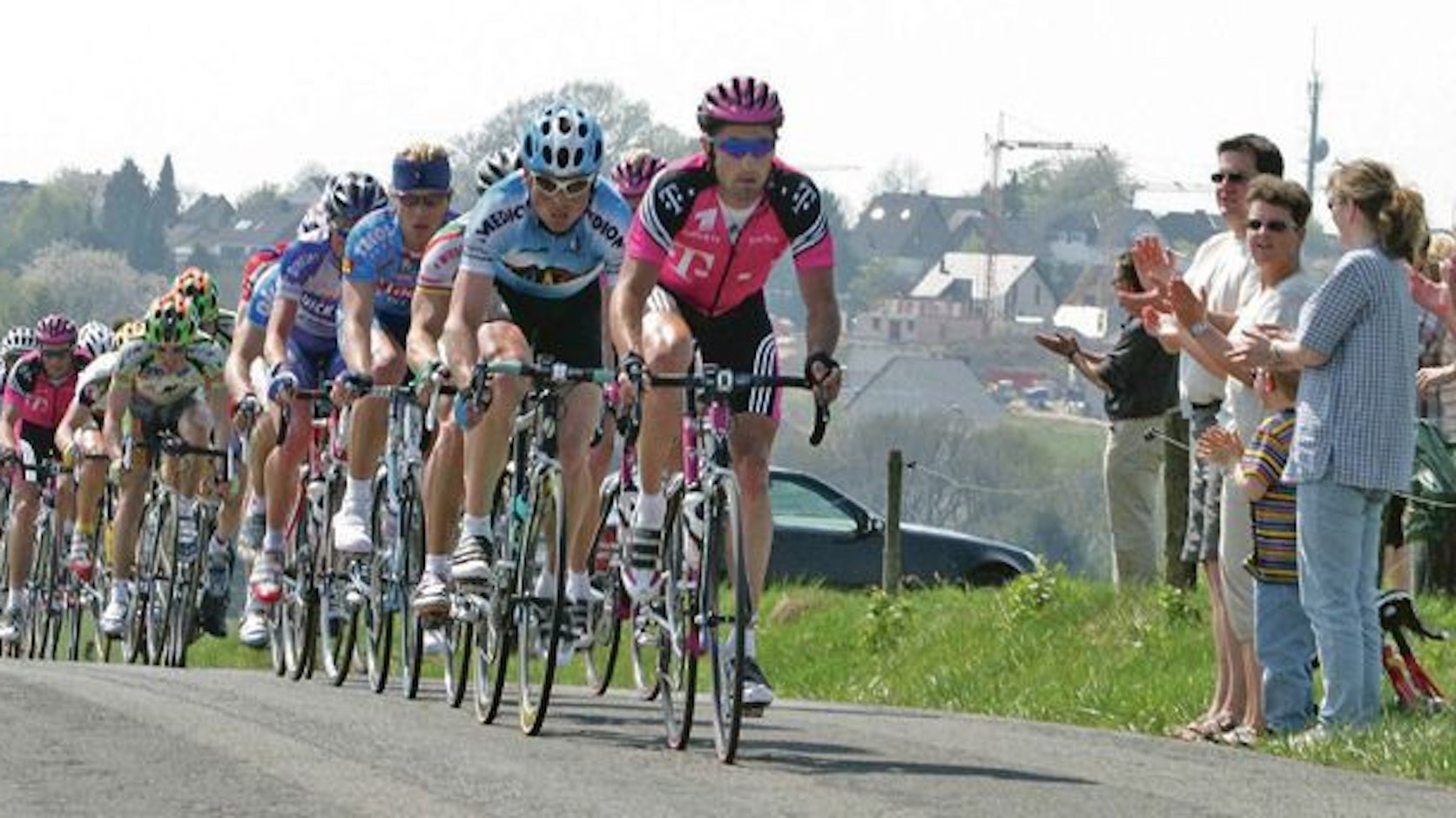 Radsportler fahren die Streckenpassage bei Heiligenhaus. Zuschauende applaudieren vom Streckenrand aus.
