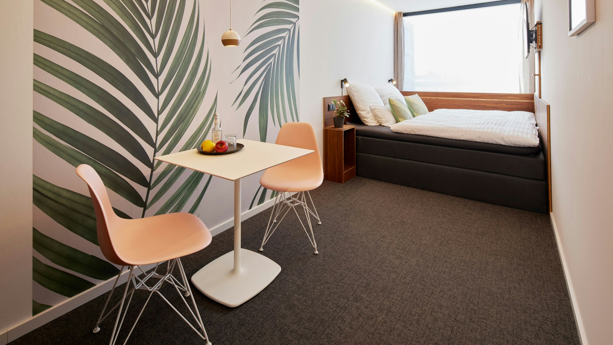 Am Ende des Raums steht ein Bett, im Vordergrund steht ein Tisch mit Stühlen.