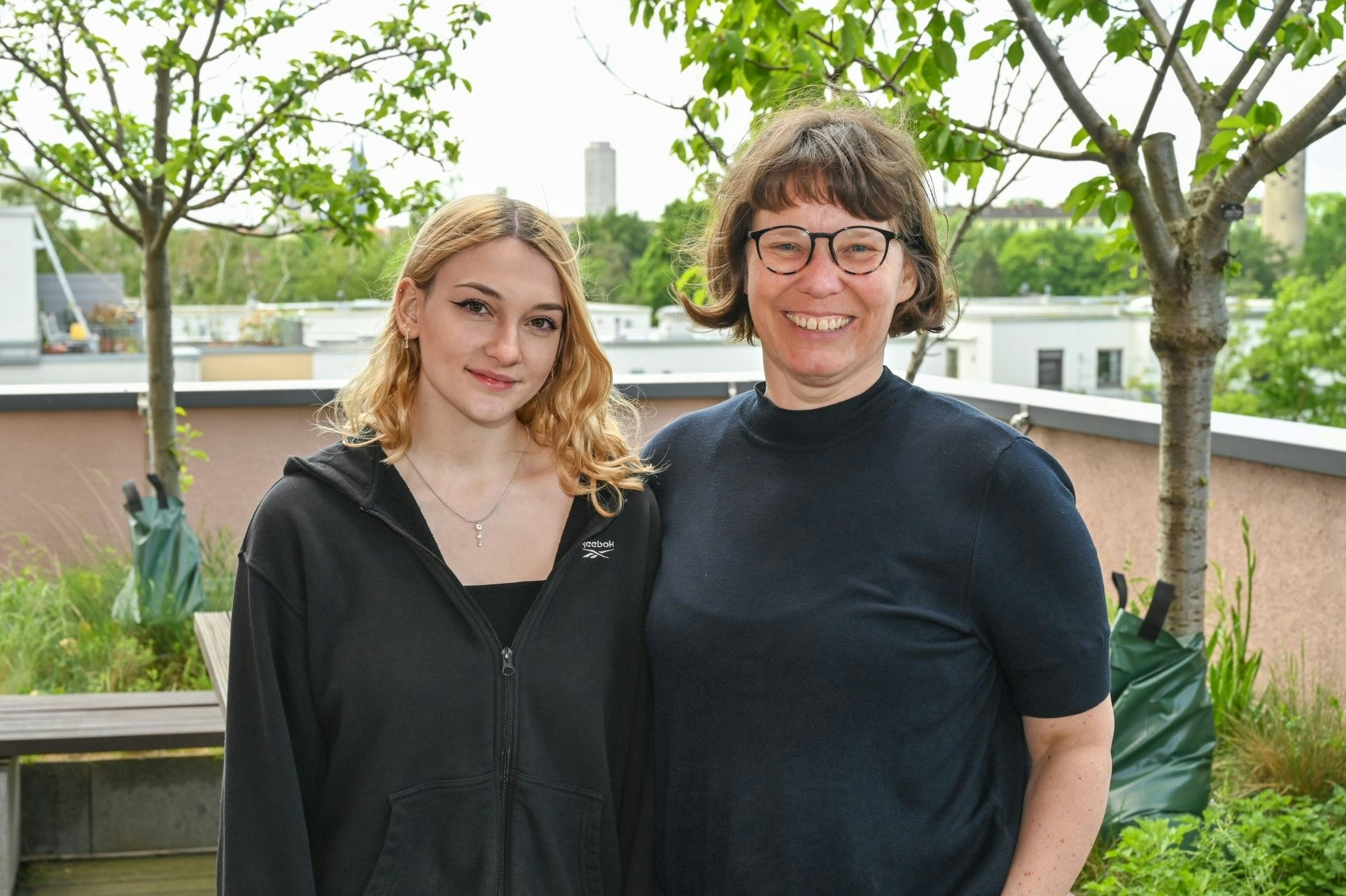 Zwei Frauen, eine junge mit blondem Haar und eine ältere mit dunklem Pagenkopf und Brille, stehen nebeneinander.