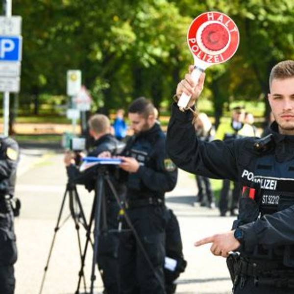 Mit einer Haltekelle winkt ein Polizist Autofahrer aus dem Verkehr.