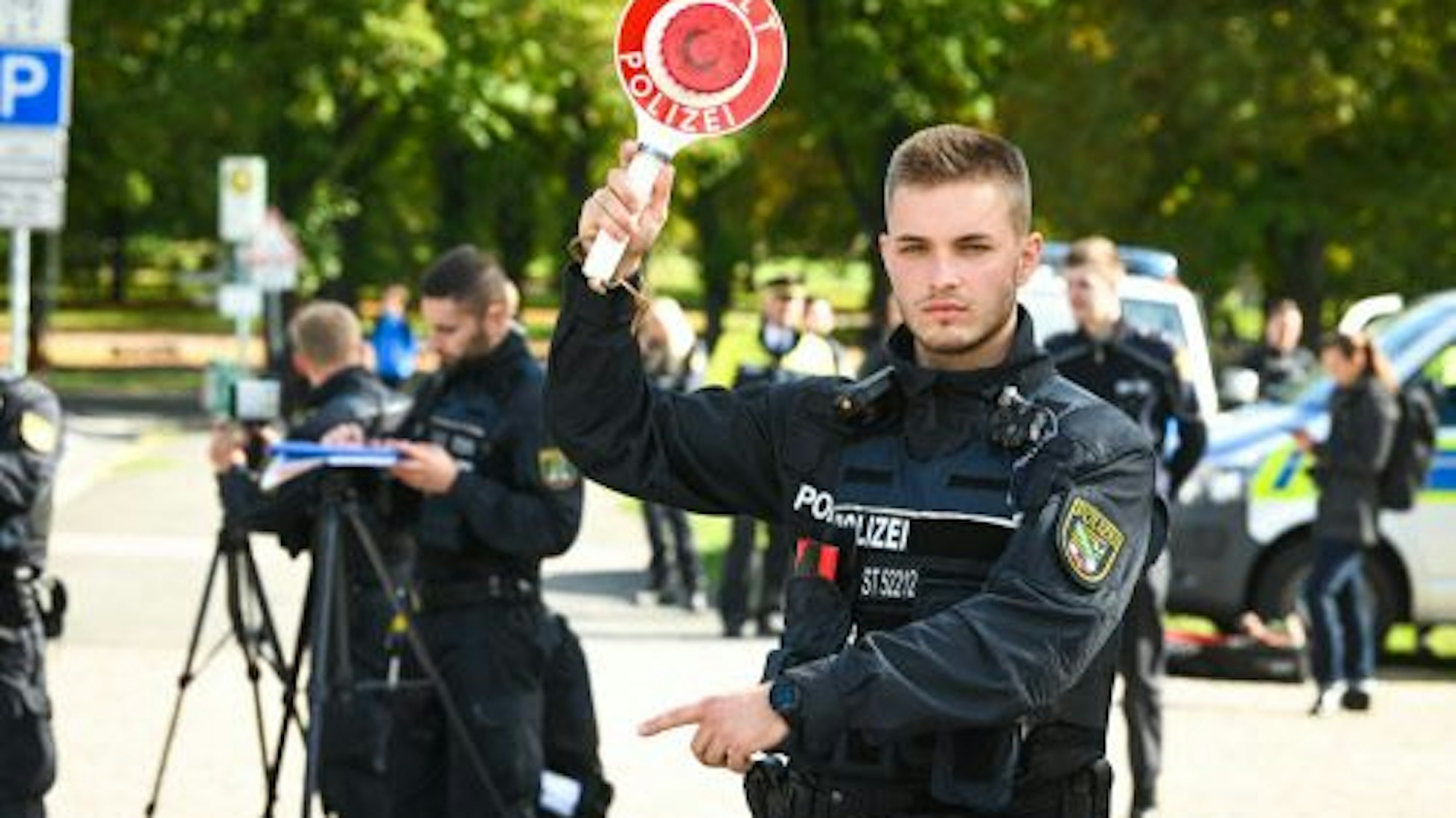 Mit einer Haltekelle winkt ein Polizist Autofahrer aus dem Verkehr.