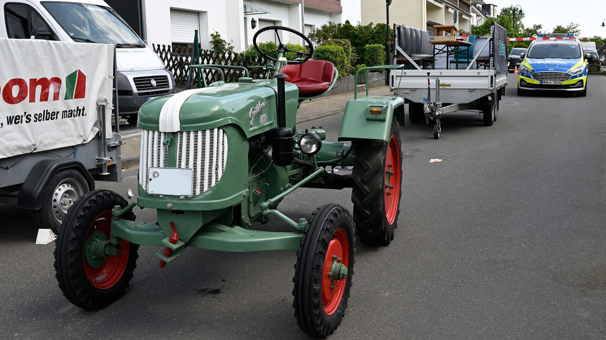 Ein Traktor steht auf einer Straße, dahinter ein abgekoppelter Anhänger, dahinter ein Polizeifahrzeug.