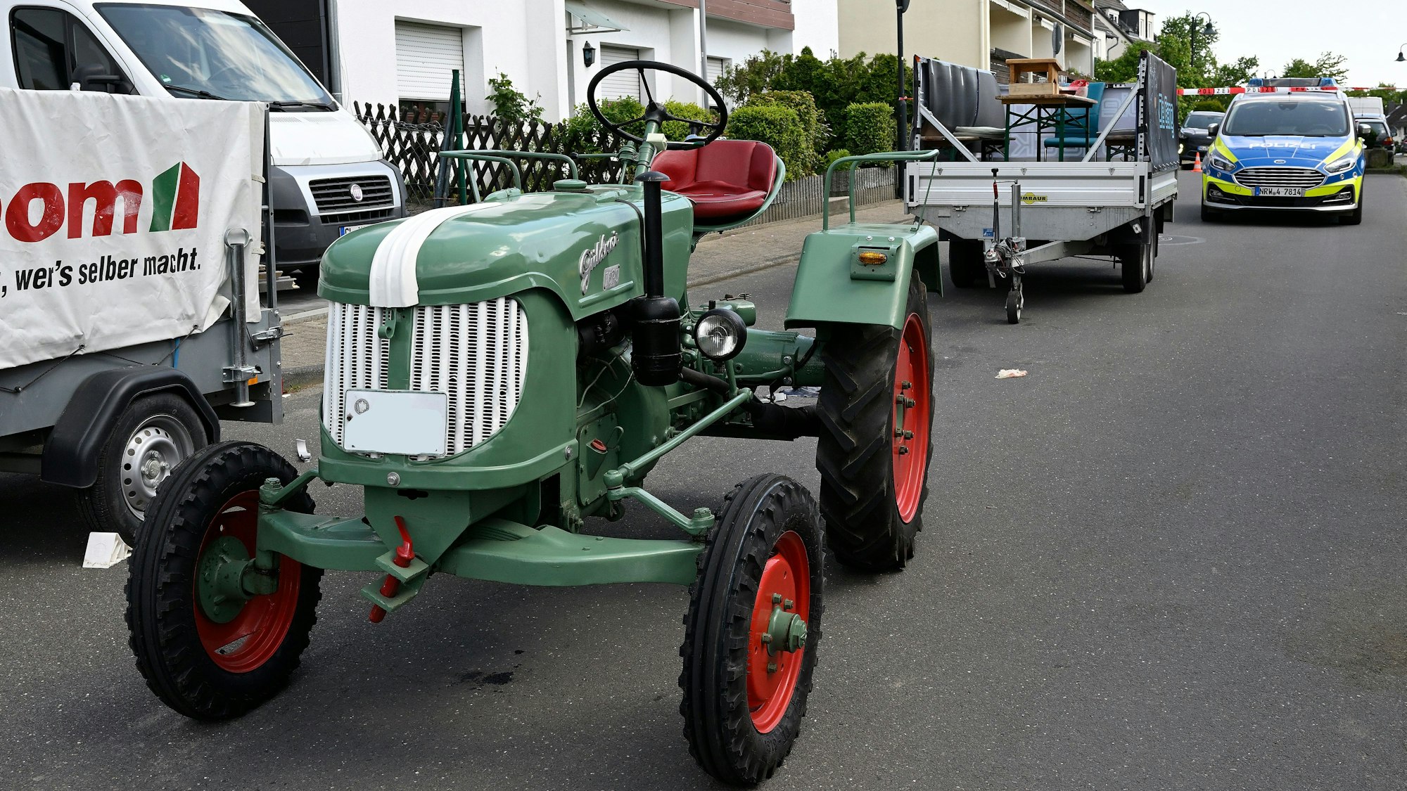 Ein Traktor steht auf einer Straße, dahinter ein abgekoppelter Anhänger, dahinter ein Polizeifahrzeug.