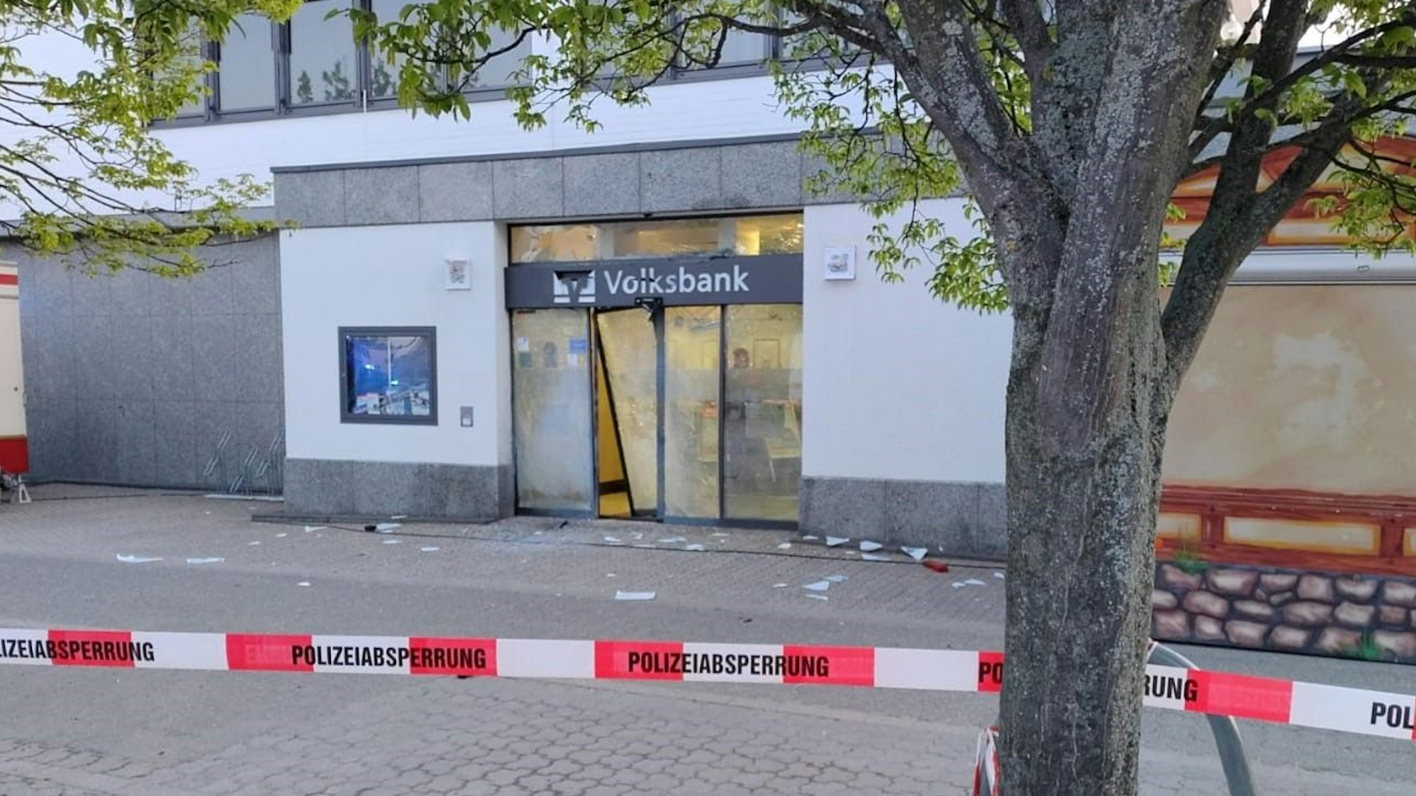 Das Bild zeigt einen von der Polizei abgesperrten Bereich, in dem die zerstörte Tür der Mechernicher Volksbank-Filiale zu sehen ist.