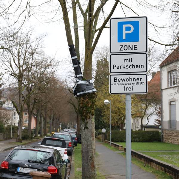 Ein Schild weist die Straße als Parkzone mit Parkschein aus, Bewohner mit Ausweis können dagegen frei parken. In der Straße stehen rechts am Fahrbahnrand parkende Autos.