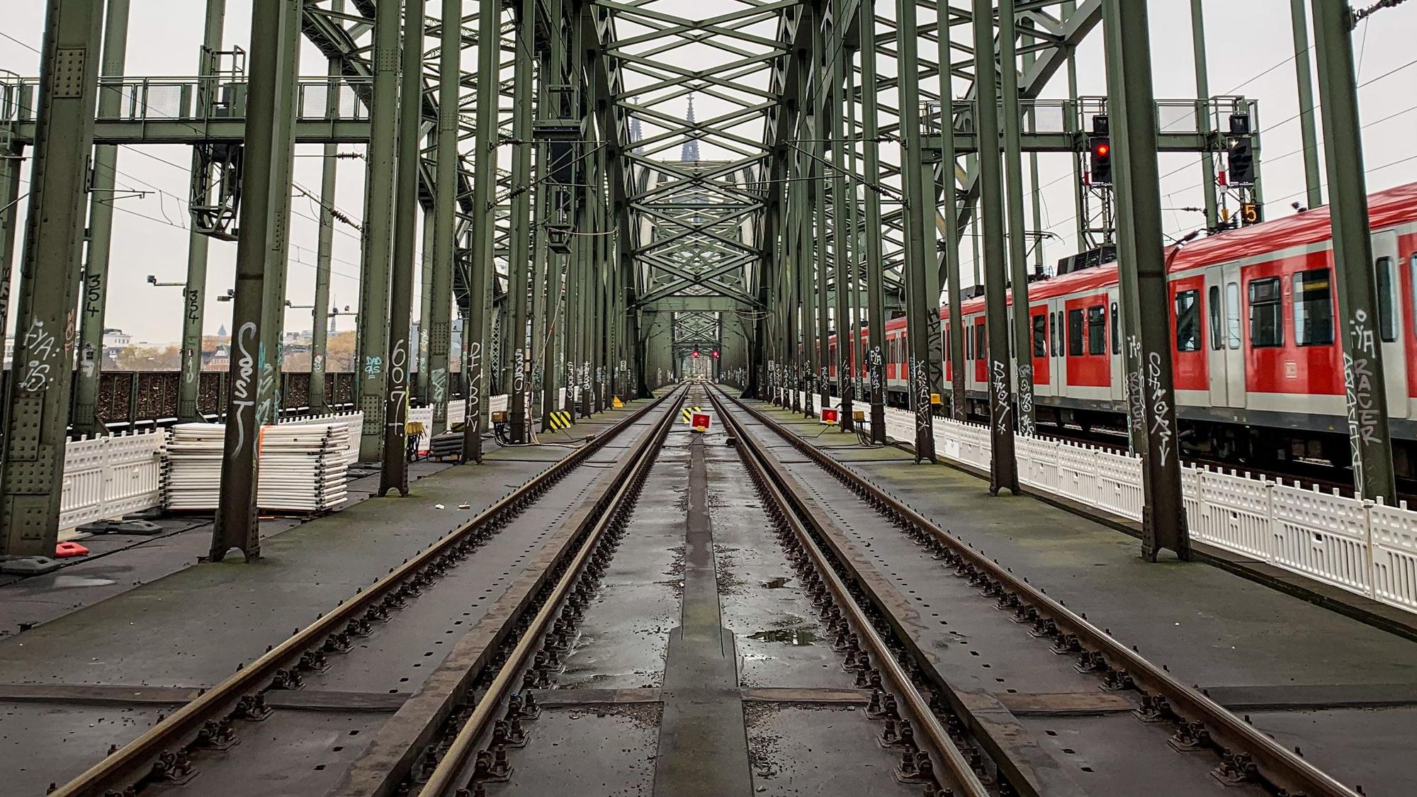 Die Gleise der Kölner Hohenzollernbrücke. Im Hintergrund ist der Kölner Dom zu sehen, rechts fährt eine S-Bahn vorbei. (Symbolbild)
