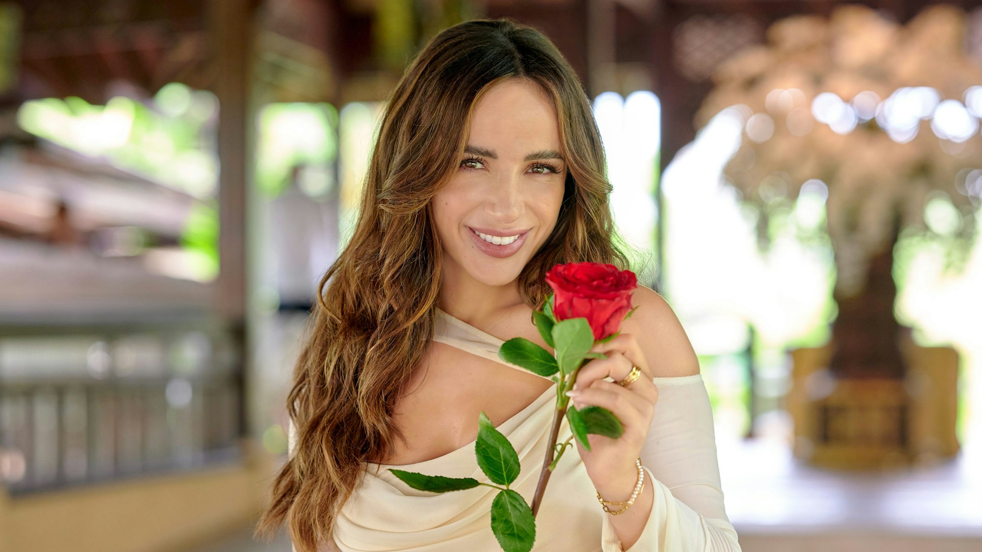 Jennifer Saro hält eine rote Rose in der Hand und lächelt in die Kamera.