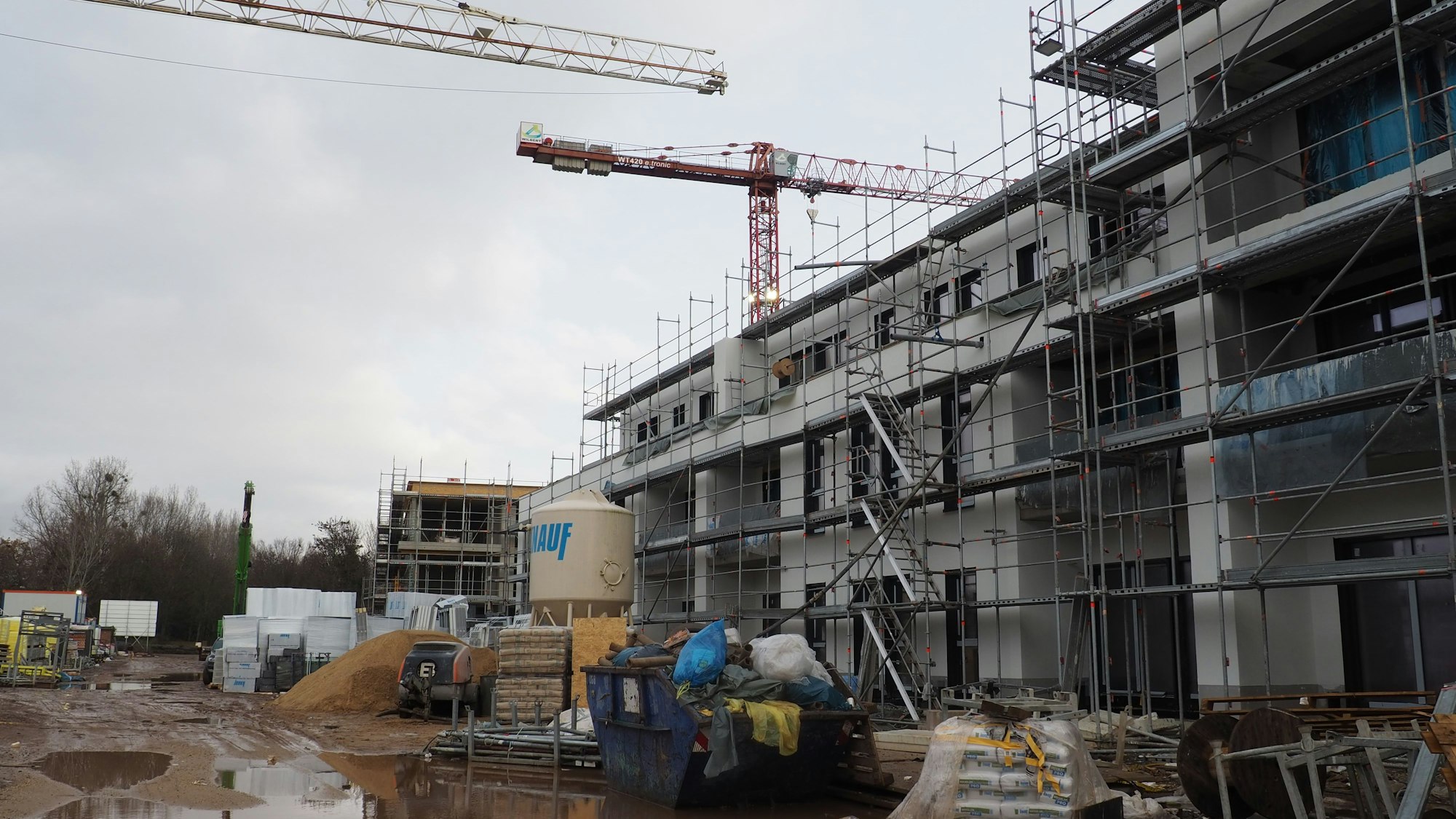 Ein Bauprojekt in Erftstadt-Konradsheim ist zu sehen. Zwei Kräne und ein dreistöckiges Haus sind Inhalt des Bildes und der Baustelle.
