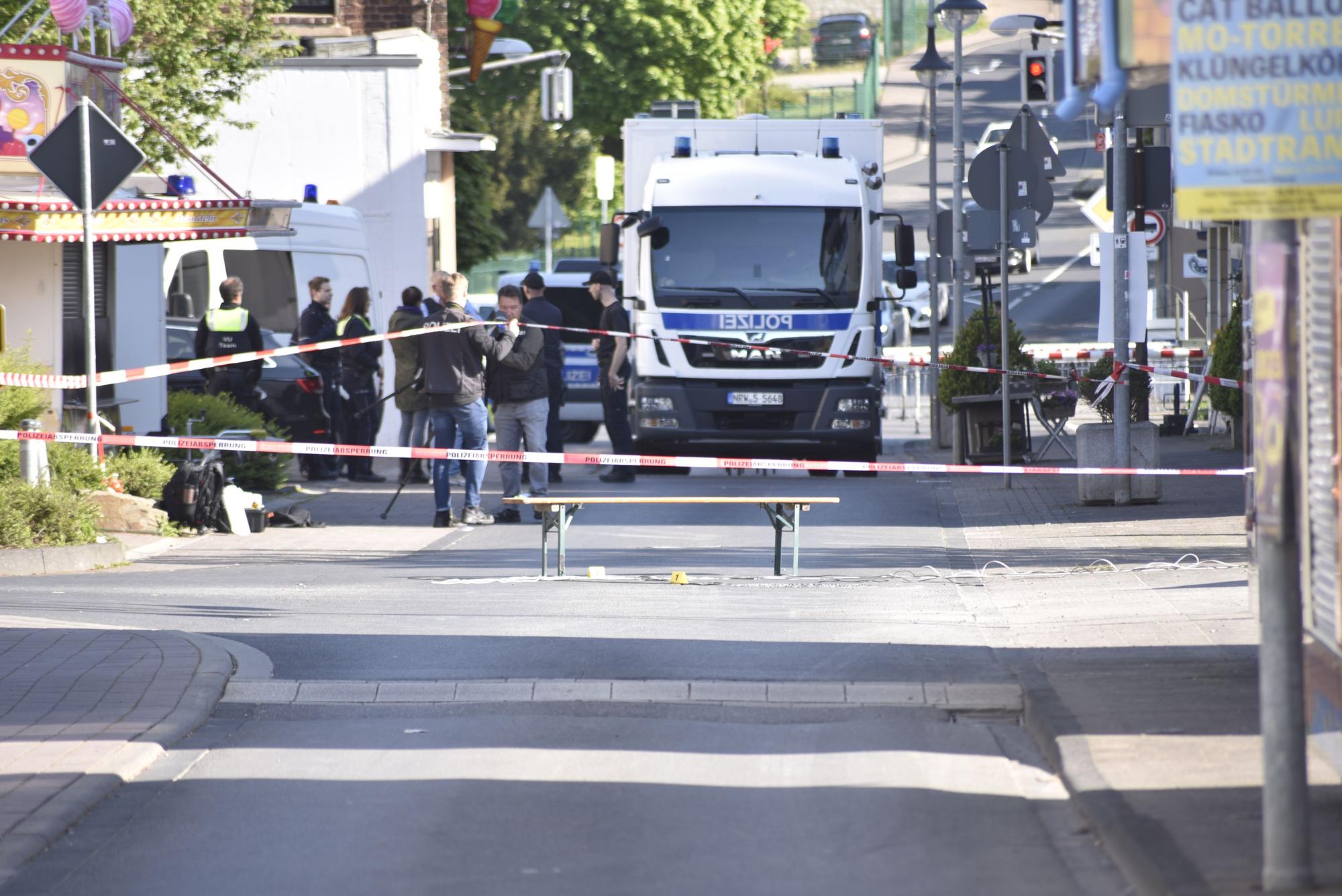 Auf der Kreuzung Weierstraße/Bergstraße in Mechernich steht eine Bierbank, davor sind Markierungen der Polizei zu sehen. Der Bereich drumherum ist mit Flatterband abgesperrt, im Hintergrund sind Polizeiwagen und Kirmesbuden zu sehen.