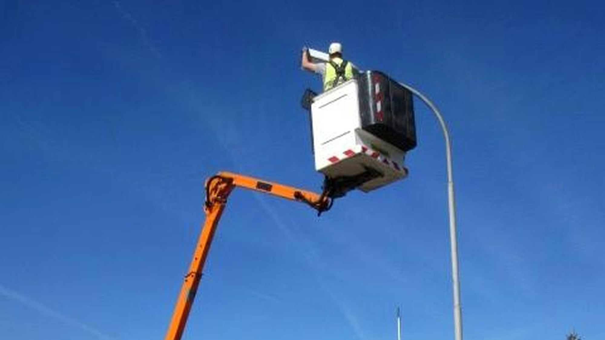 Eine Umrüstung einer Straßenlampe in Kall ist abgelichtet. Ein Mensch wird von einem Kran hoch zur Lampe gehievt und arbeitet an dieser.