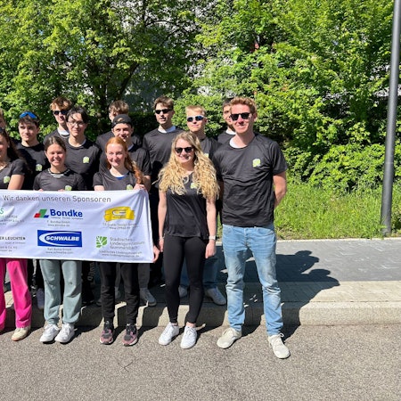 Eine Gruppe Schülerinnen und Schüler steht mit einem Sponsoren-Banner zusammen.