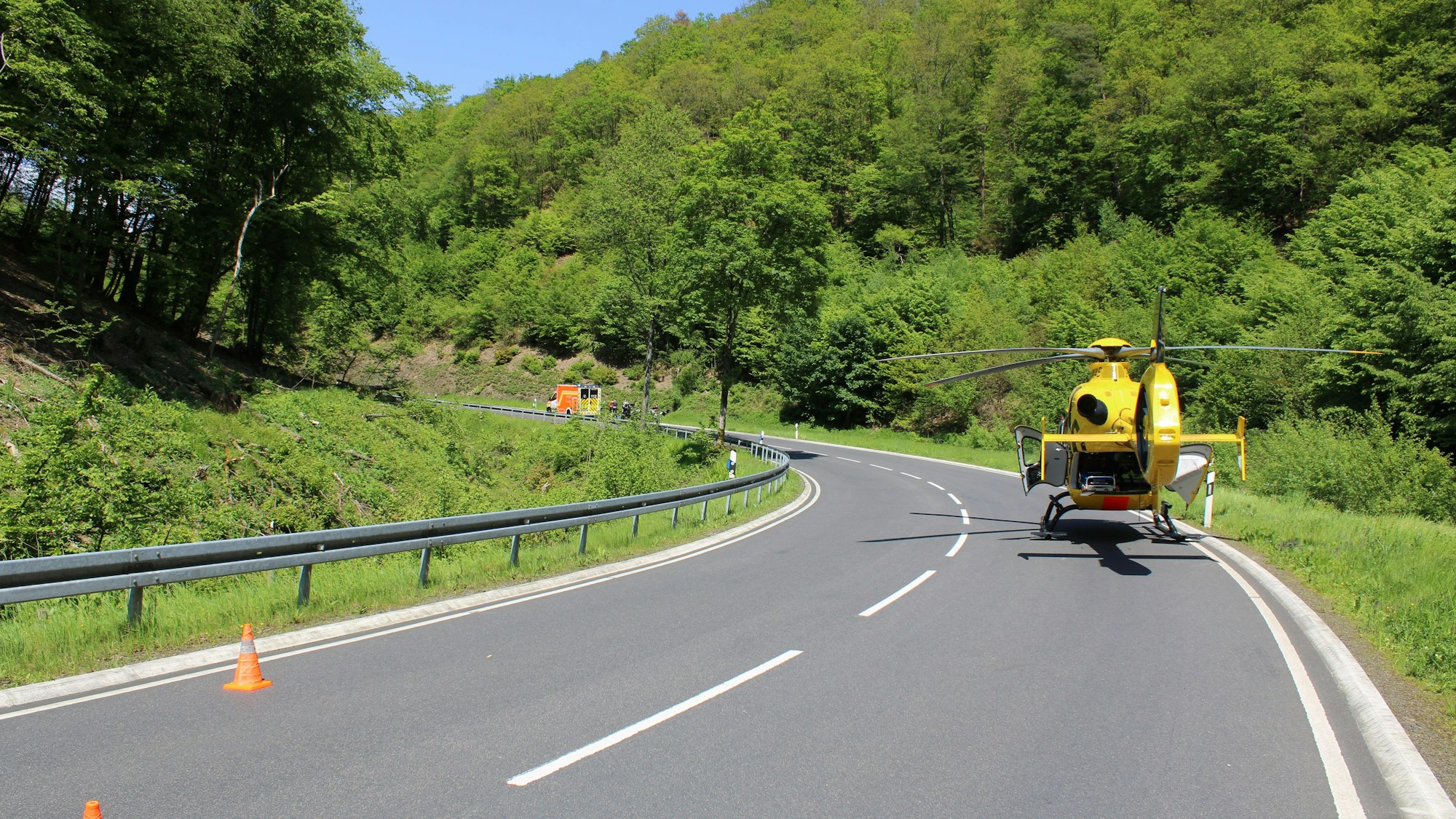 Es ist die Strecke zu sehen. Auf der Straße steht ein Rettungshubschrauber, in der Ferne ein Krankenwagen.