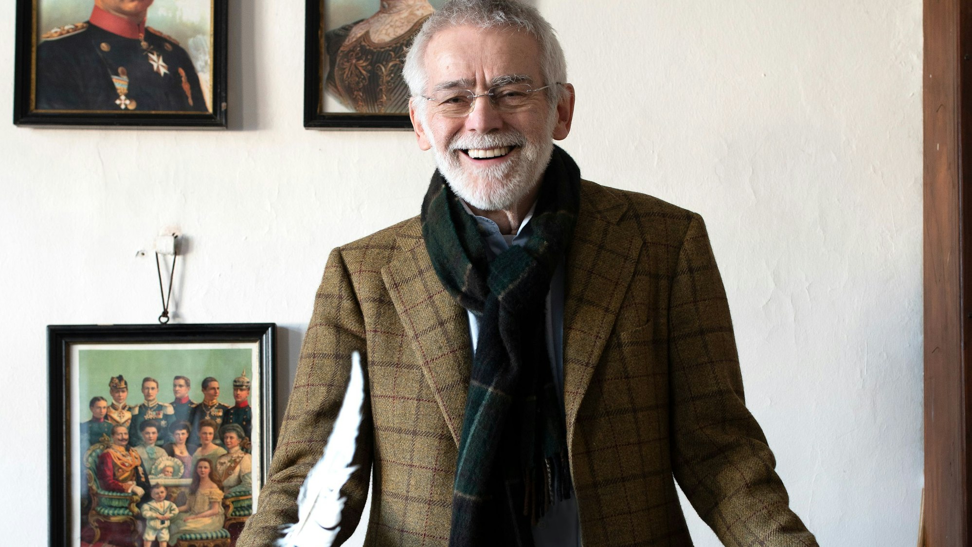 Dr. Peter Joerißen, Leiter Schulmuseum Bergisch Gladbach, im alten Klassenzimmer der ehemaligen Volksschule. Er steht vor einigen Gemälden, die an einer weißen Wand hängen, und lächelt an der Kamera vorbei.