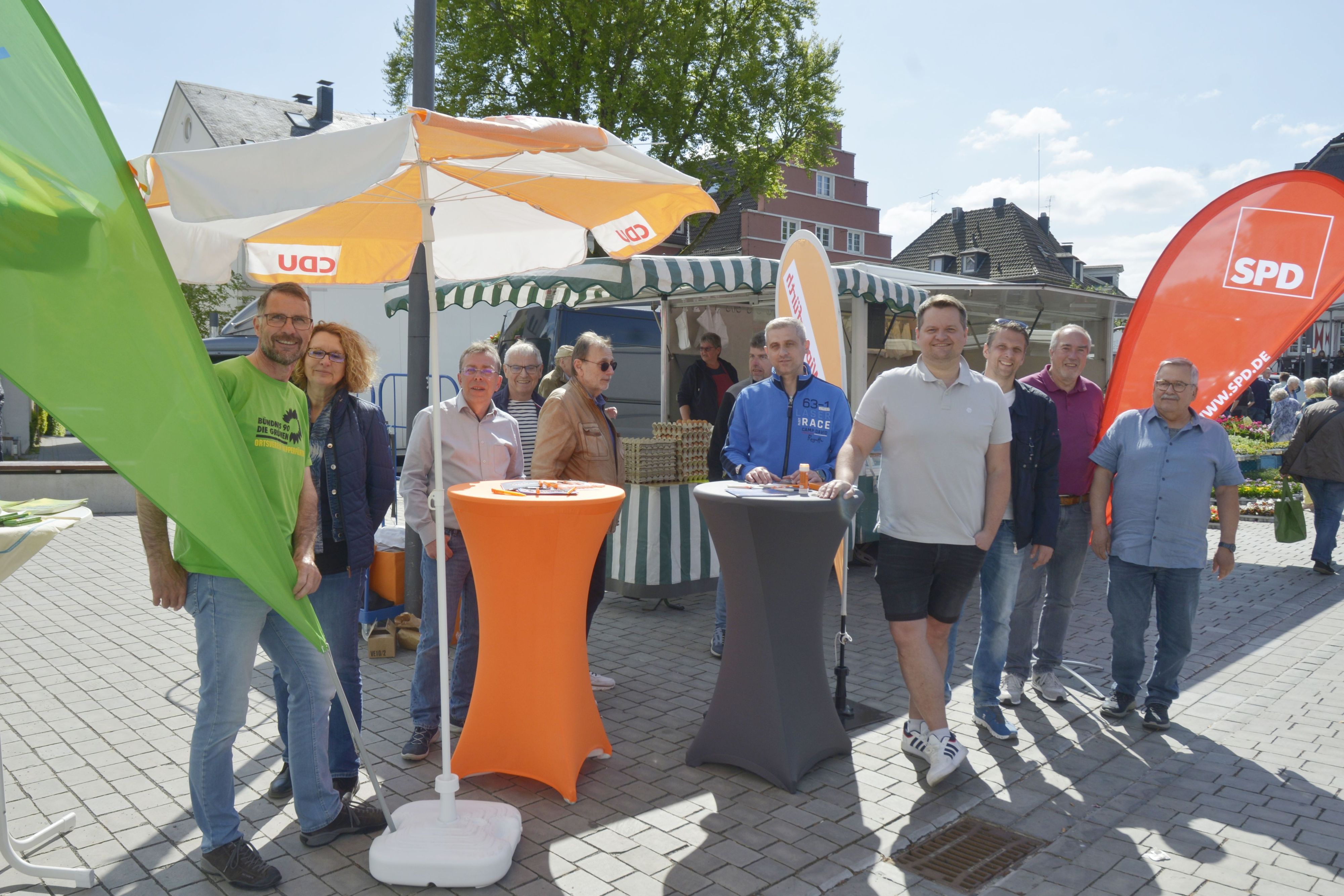 Es sind mehrere Mitglieder der drei Parteien zu sehen, wie sie vor ihren ständen stehen.