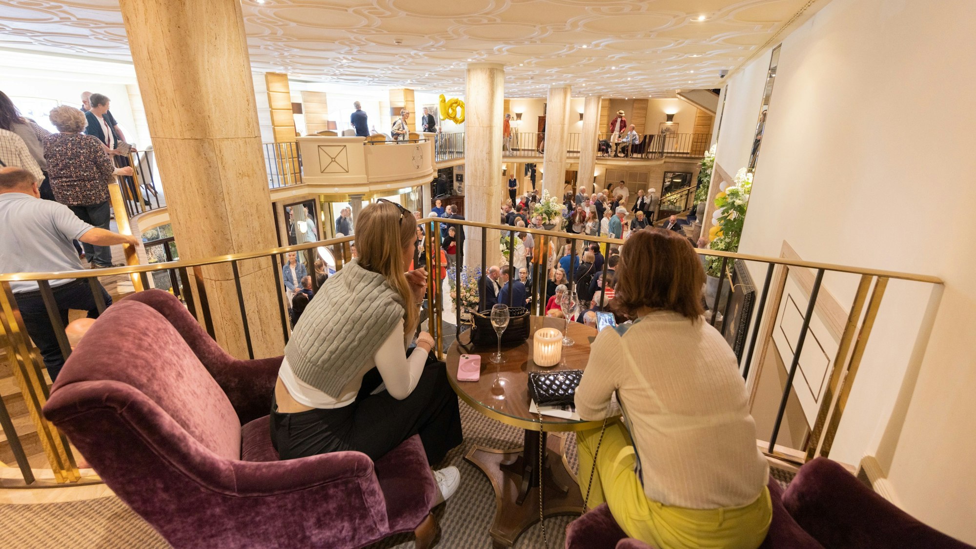 Viele Menschen sammeln sich in einer Hotellobby, die aus einem höheren Stockwerk zu sehen ist.