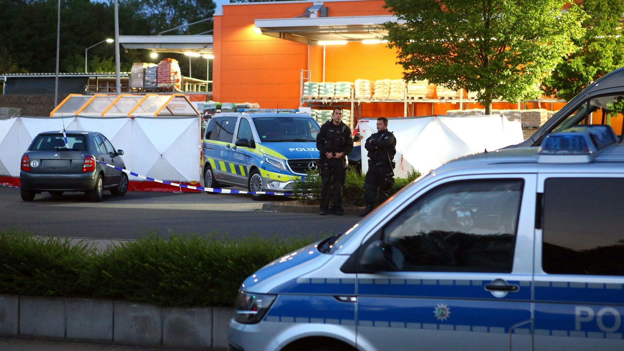 Polizisten stehen am Tatort auf dem Parkplatz eines Aachener Baumarkts.
