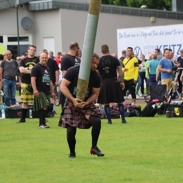 Das Bild zeigt einen Mann im Kilt, der einen Baumstamm in die Höhe hievt.