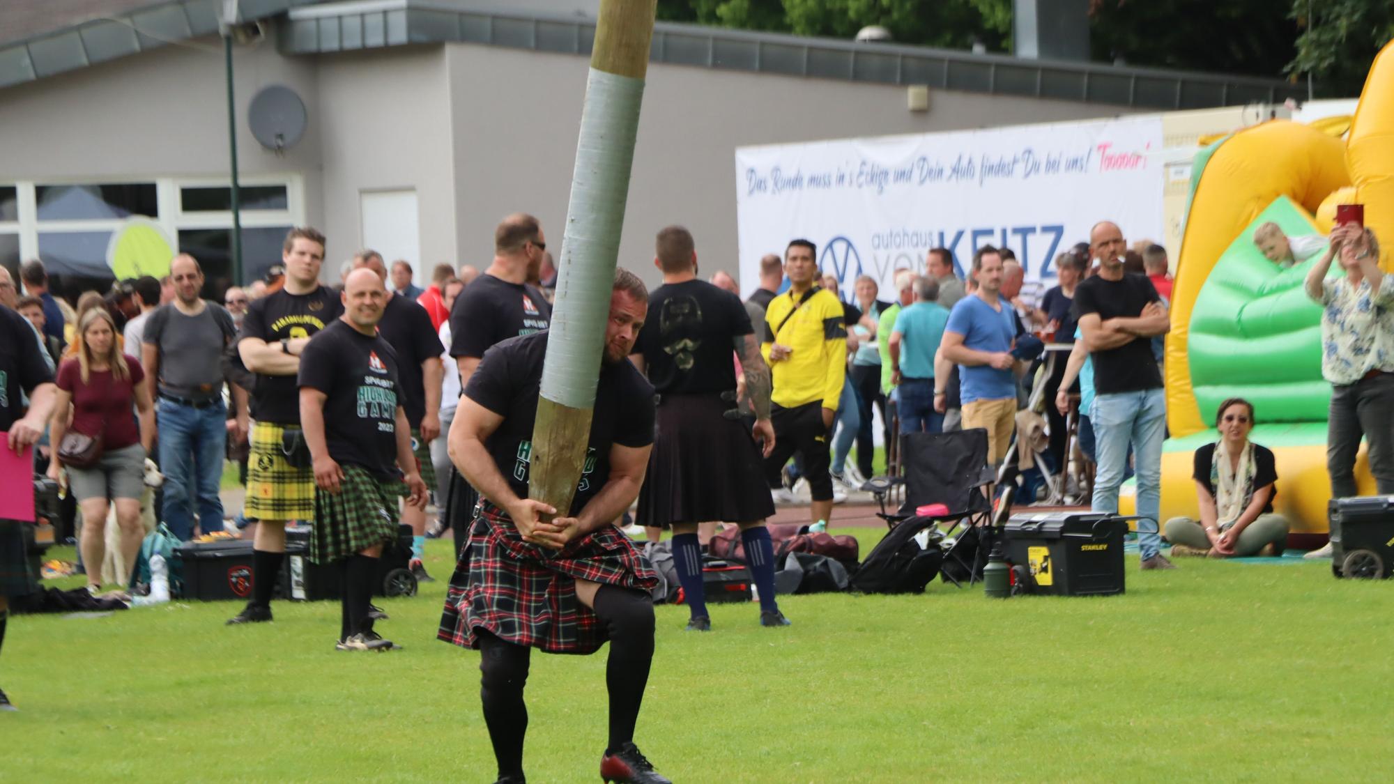 Das Bild zeigt einen Mann im Kilt, der einen Baumstamm in die Höhe hievt.
