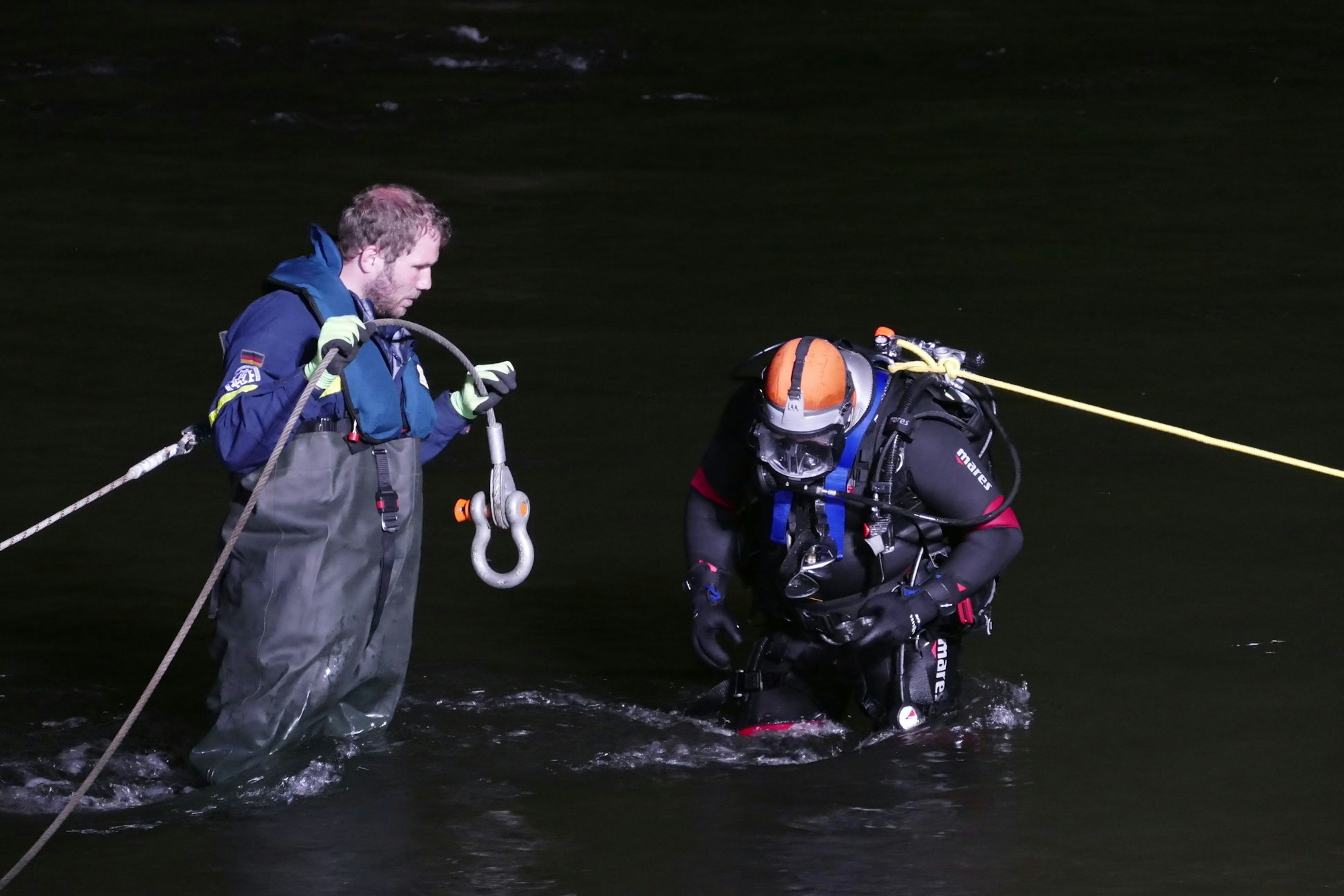 Zwei Taucher an Leinen sind dabei, Haken an einem unterwasser liegenden Tank anzulegen.