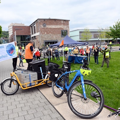 Zu sehen sind in gelbe Westen gekleidete Radfahrer, die sich versammeln und Transparente hochhalten.