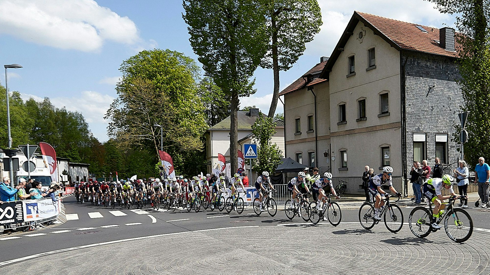 Ein Pulk Rennradfahrer wird vom Publikum mit Beifall begrüßt.