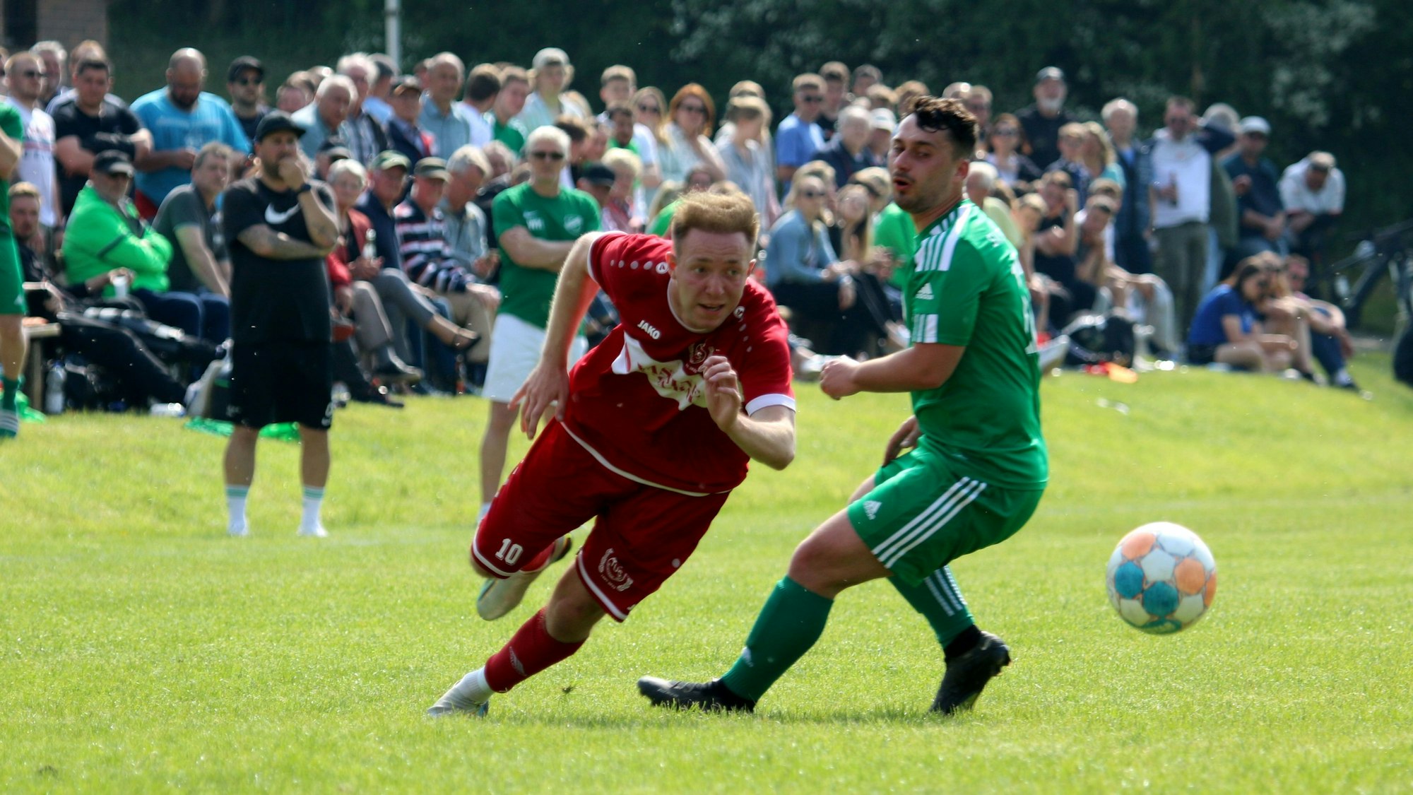 Mechernichs Jonas Hohn sprintet an Sötenichs Marvin Neumann vorbei. Im Hintergrund sieht man neben den Sötenicher Verantwortlichen viele Zuschauer.