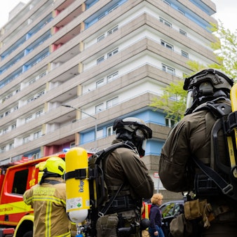 11. Mai: Polizeibeamte mit Gasmasken und Feuerwehrleute stehen vor dem Hochhaus in Ratingen, wo ein 57-Jähriger bewusst eine Explosion herbeigeführt haben soll.