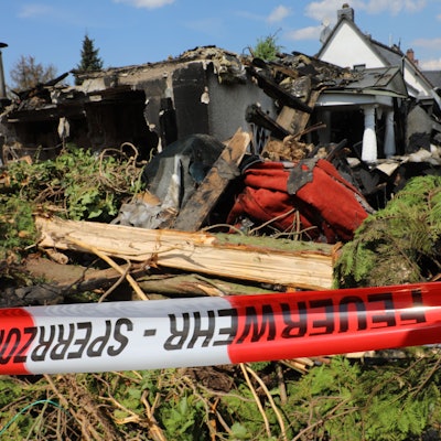 Vor dem abgebrannten Haus hängt ein Absperrband.