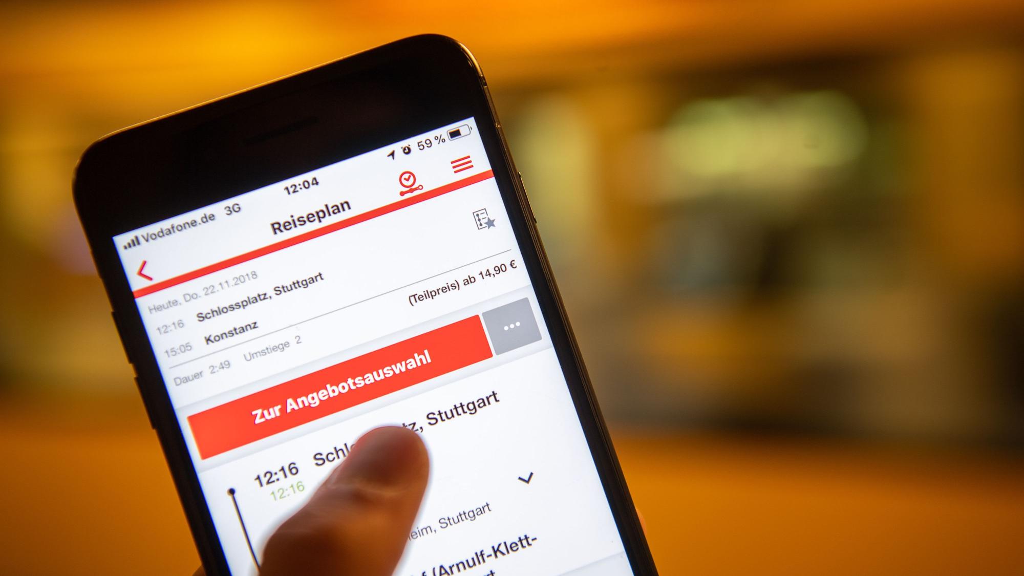 Ein Mann hält ein Smartphone in der Hand, auf dem der DB Navigator mit der Suche nach einer Fahrt von Stuttgart nach Konstanz zu sehen ist.