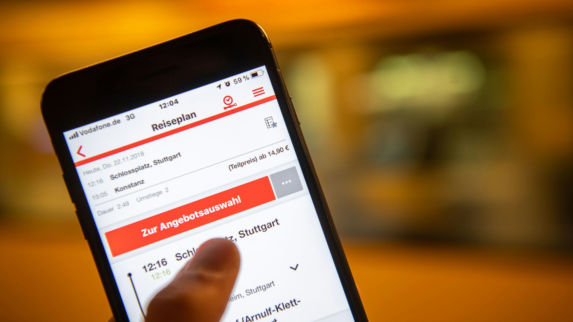 Ein Mann hält ein Smartphone in der Hand, auf dem der DB Navigator mit der Suche nach einer Fahrt von Stuttgart nach Konstanz zu sehen ist.