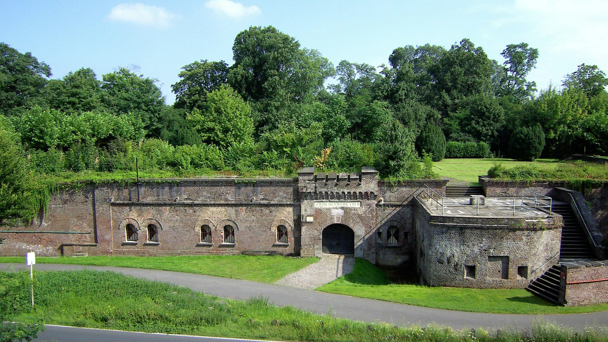 Zu sehen ist ein festungsähnlicher Bau mit viel Grün drumherum.