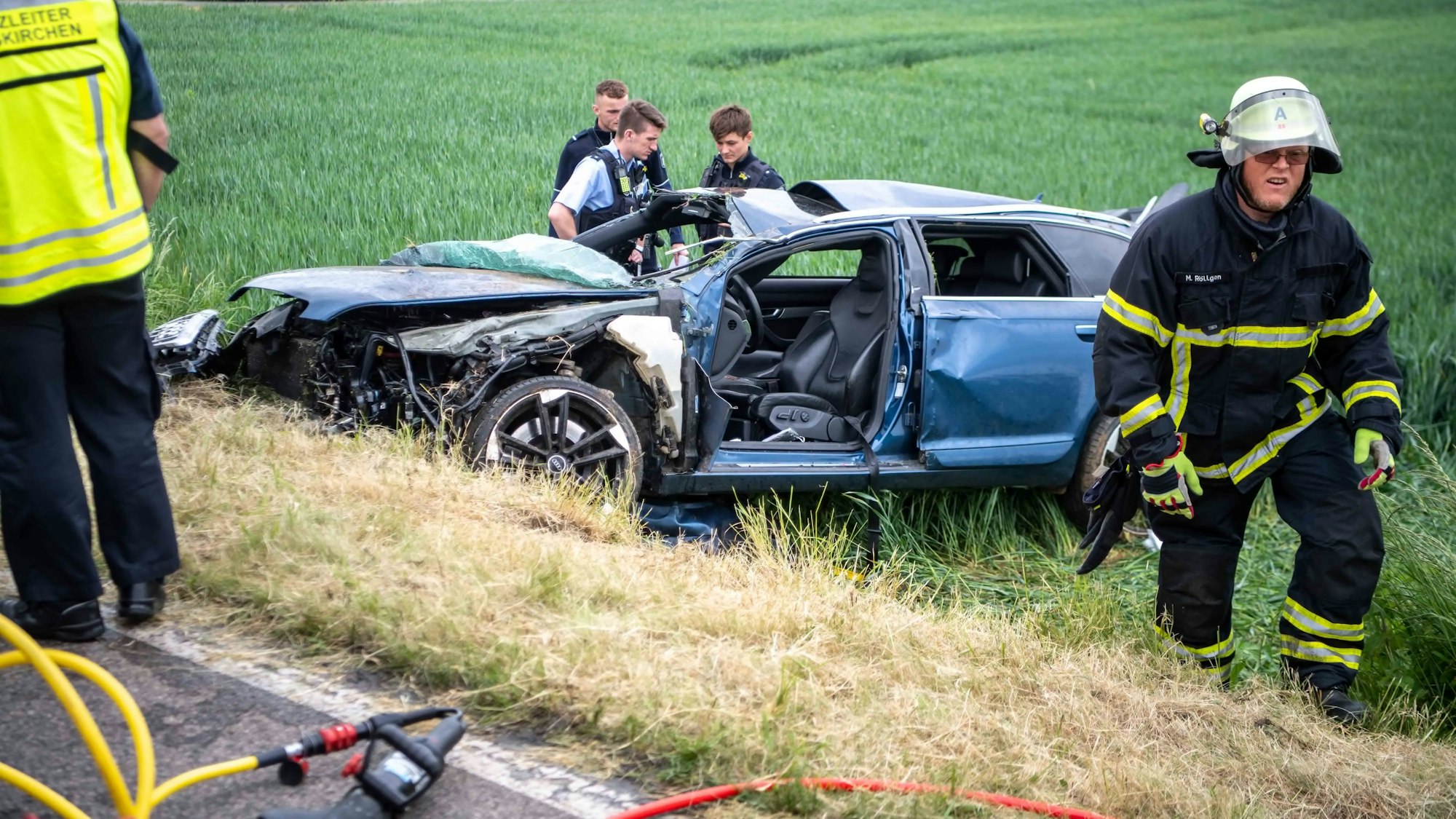 Drei Polizisten begutachten den zerstörten Audi. Auch die Feuerwehr war nach Unfall bei Kleinbüllesheim im Einsatz.