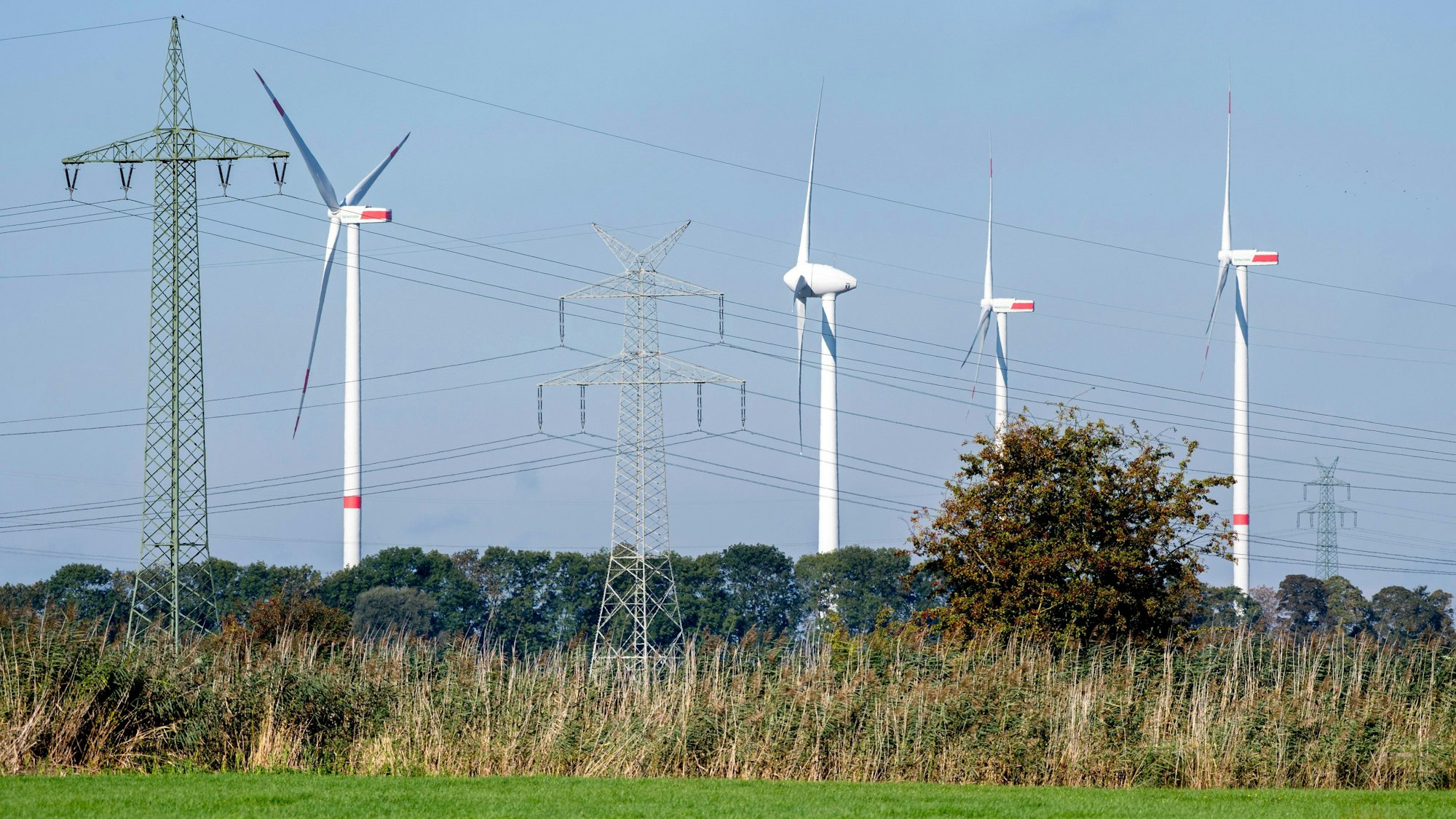 Mehrere Windkraftanlagen stehen neben einer Hochspannungsleitung und drehen sich im Wind.
