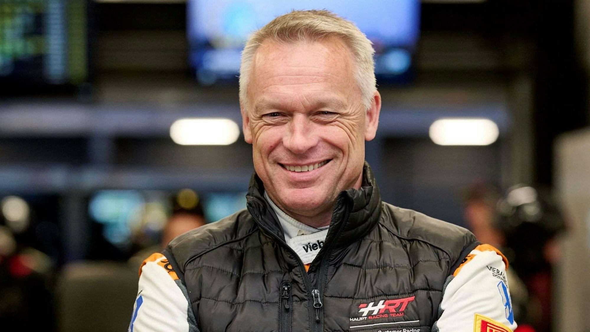 Zu sehen ist ein Rennfahrer ohne Auto und Helm.