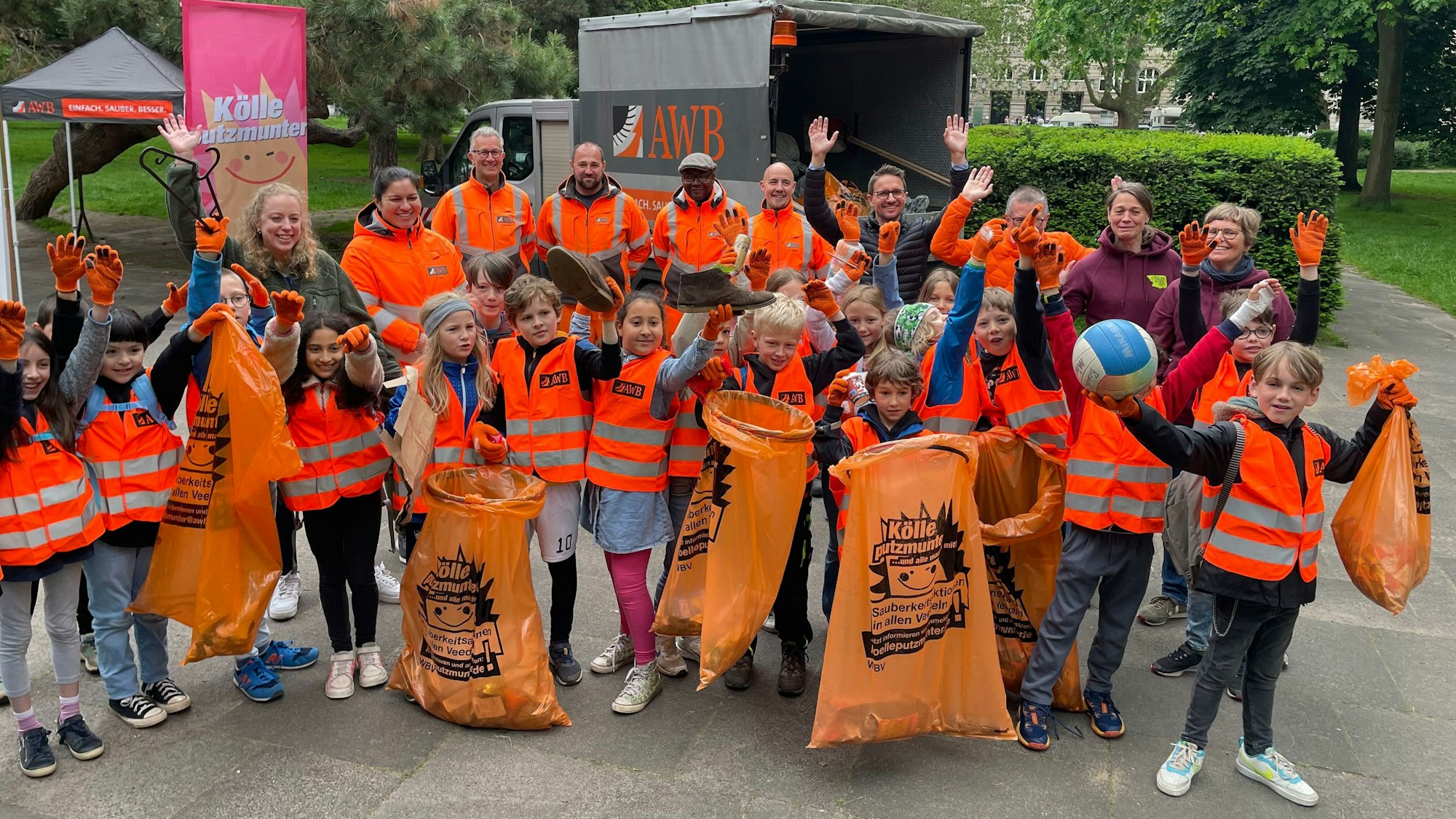 20 Grundschüler und Grundschülerinnen, Mitarbeitende der AWB und Pädagoginnen präsentieren fröhlich ihre Fundstücke, wie einen Volleyball und Schuhe