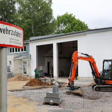 Ein Bagger gräbt vor einer Fahrzeughalle der Feuerwehr.