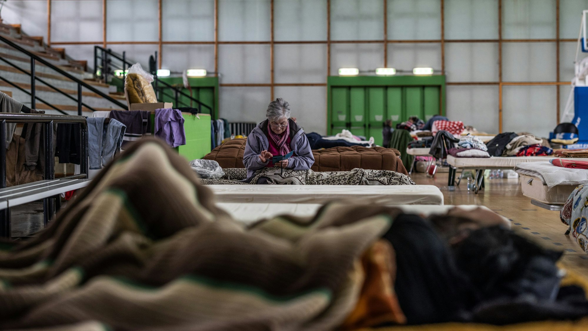 Eine ältere Frau sitzt auf einem Bett in einer Turnhalle, die als Unterkunft für Flutopfer dient.
