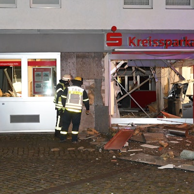 Feuerwehrleute stehen vor dem völlig zerstörten Eingangsbereich der Kreissparkasse in Kerpen-Türnich.
