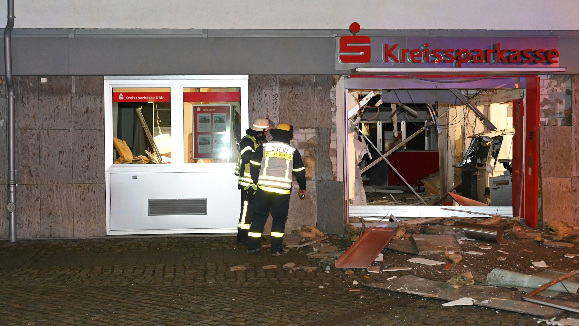 Feuerwehrleute stehen vor dem völlig zerstörten Eingangsbereich der Kreissparkasse in Kerpen-Türnich.