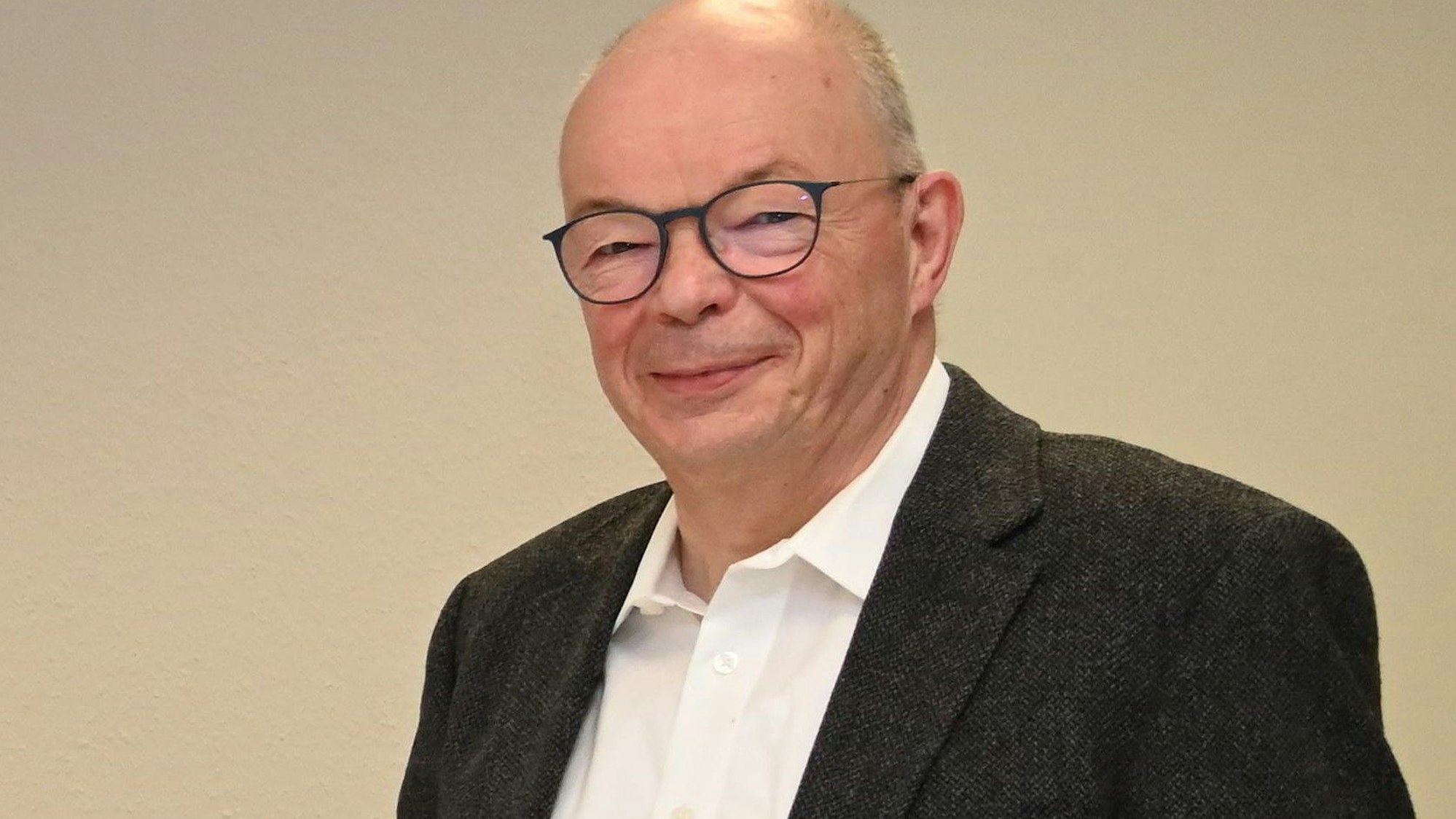 Michael Schulte steht vor einer beigen Wand und schaut in die Kamera.