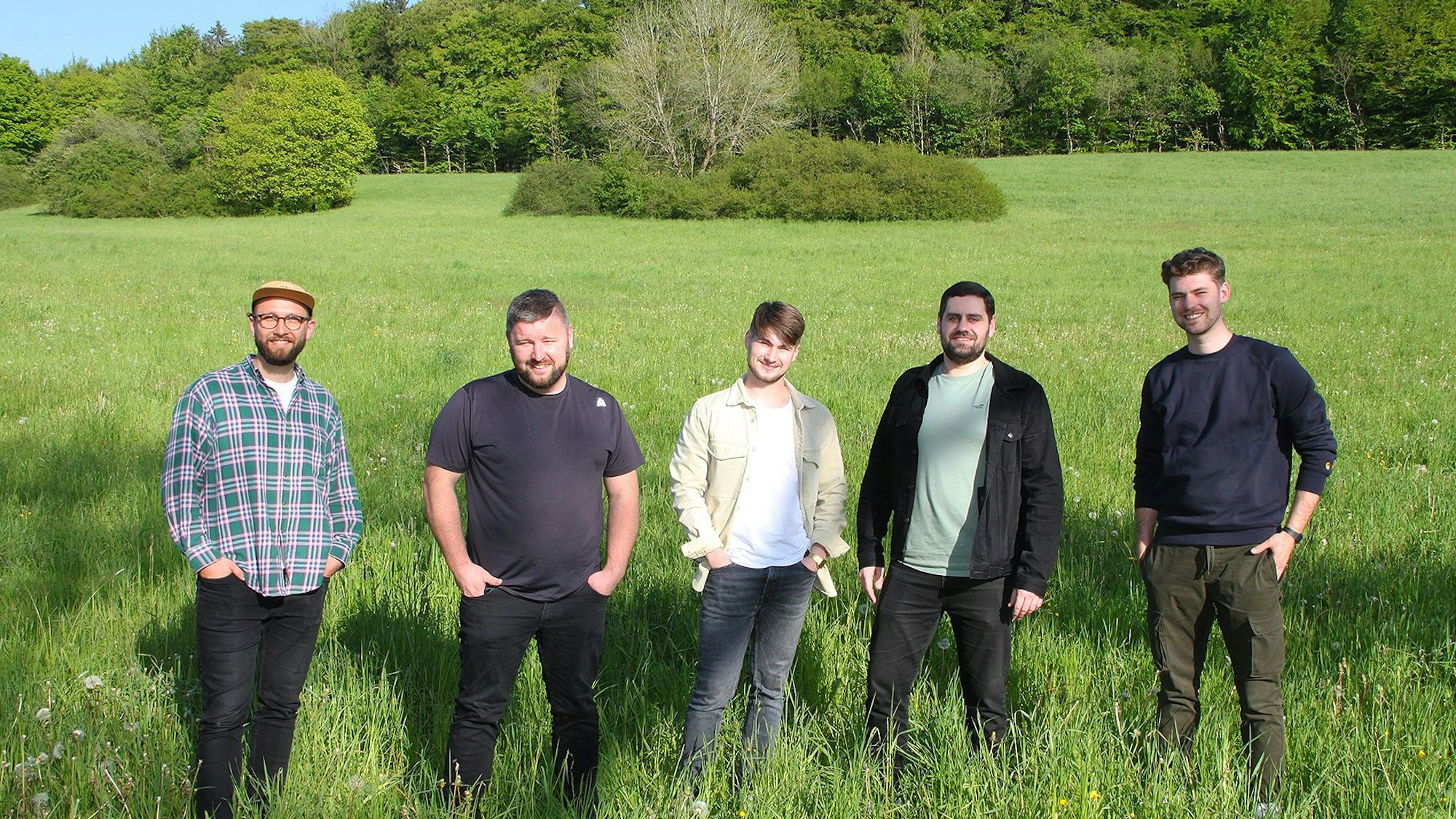 Das Bild zeigt die fünf jungen Musiker der Band „Amie & Me“ auf einer grünen Wiese.