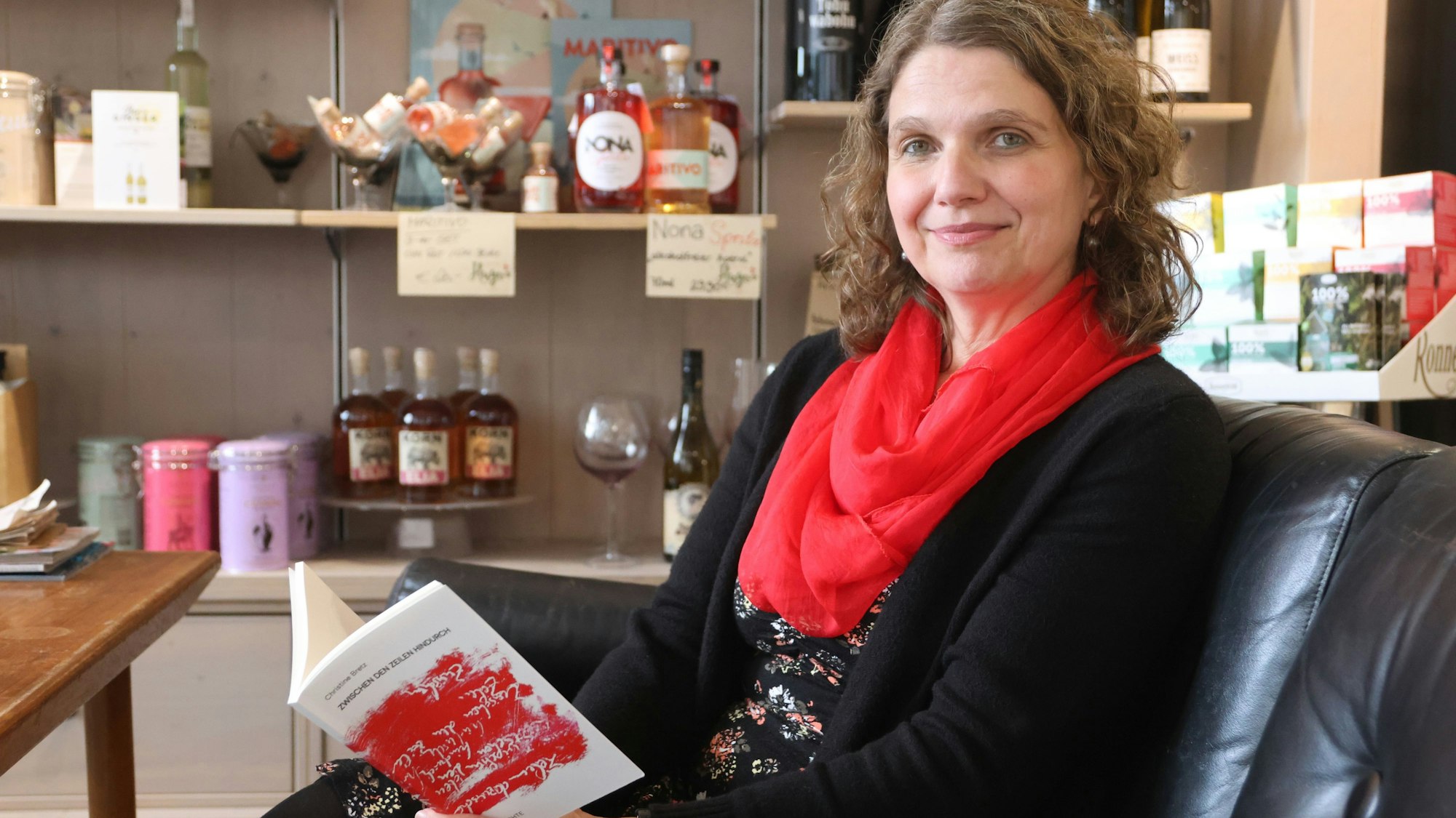 Eine Frau sitzt in einem Sessel und hält ein aufgeschlagenes Buch in der Hand.