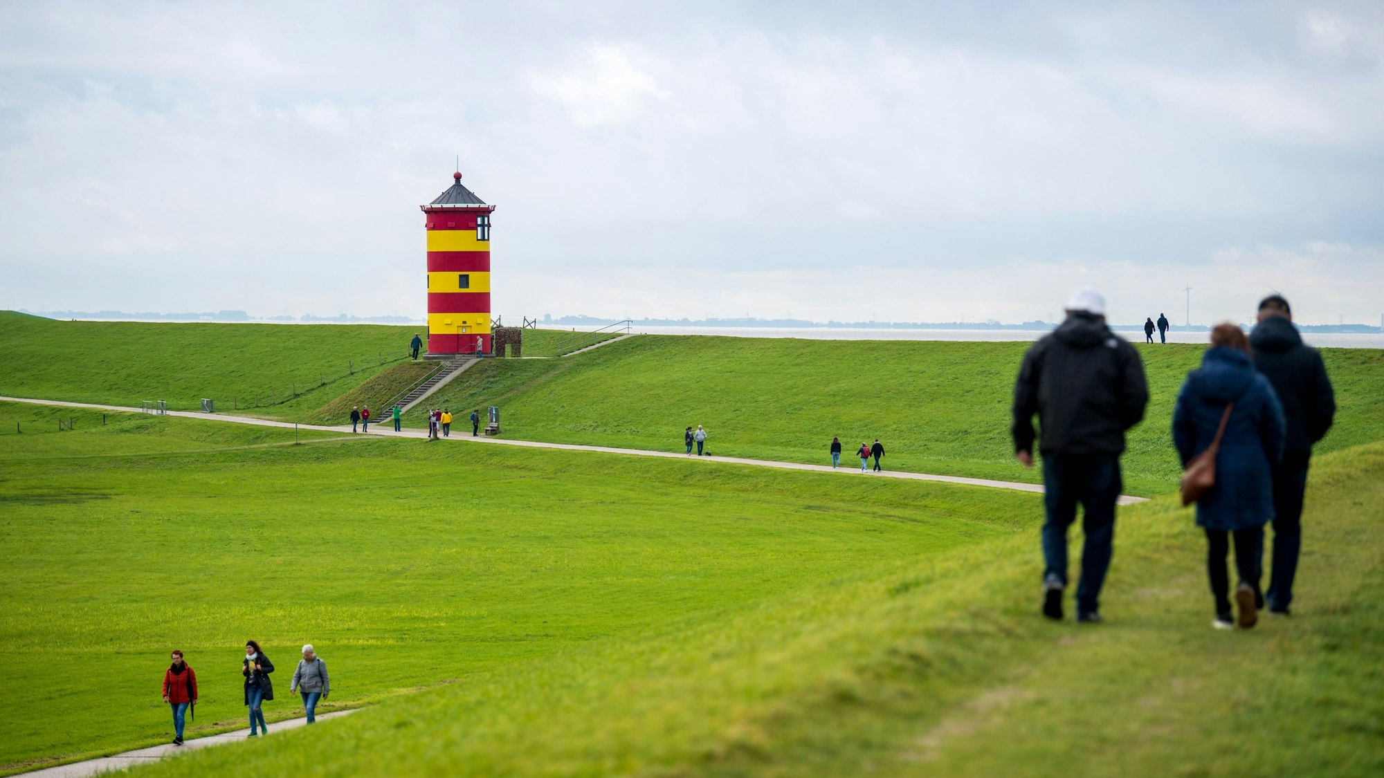 Spaziergänger laufen über den Deich vor dem Pilsumer Leuchtturm. Eine Fliegenplage gibt es derzeit an der Nordseeküste. (Symbolbild)