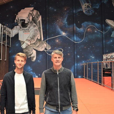 Zwei Männer stehen im Kinderland Aktivi vor einer mit Weltraum-Motiven bemalten Wand.